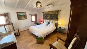 Un dormitorio con cama, una silla, una lámpara, un cuadro y una ventana.