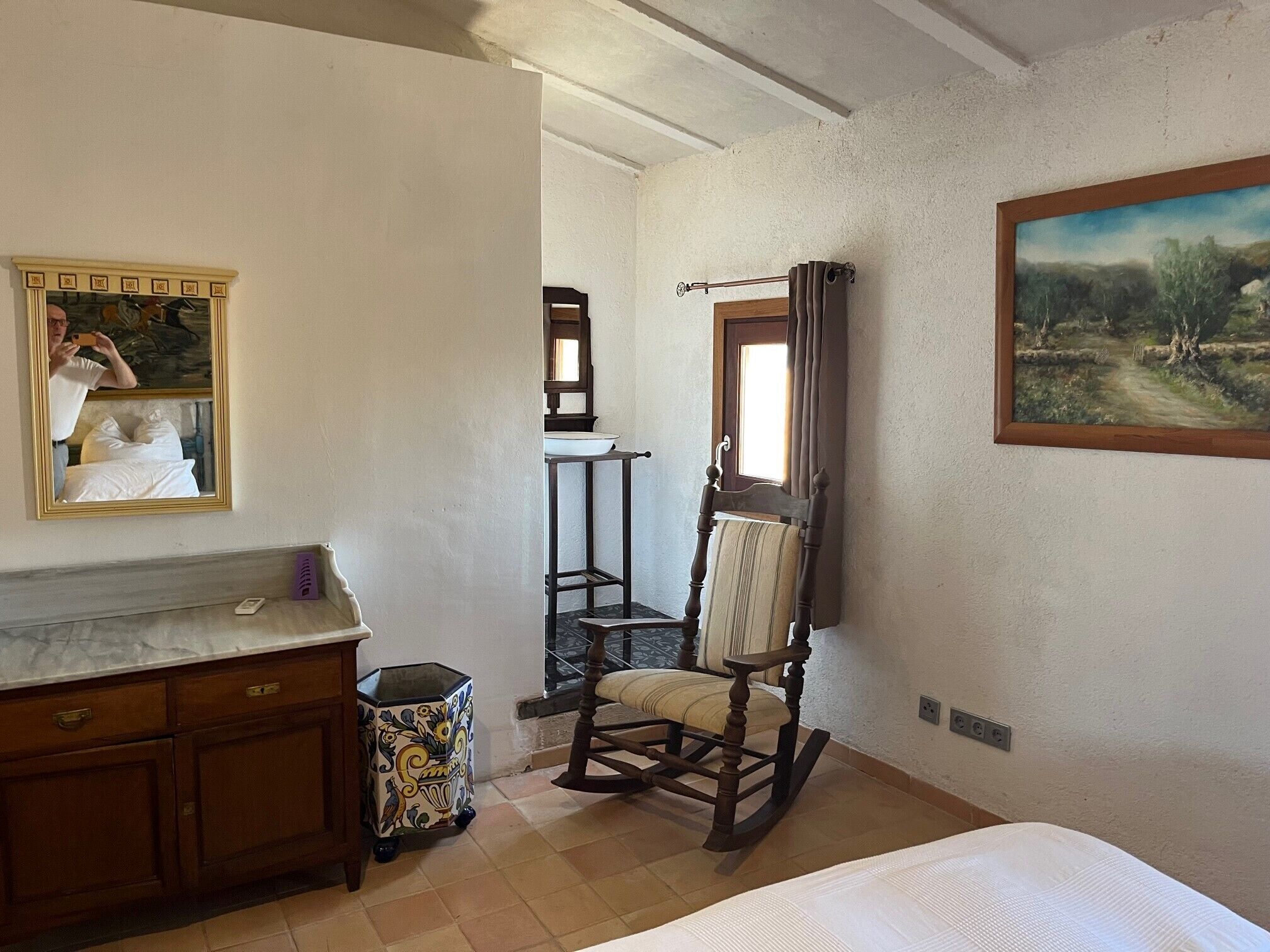 Une chambre à coucher avec un lit, un fauteuil à bascule en bois, une commode, un miroir et un tableau accroché au mur.
