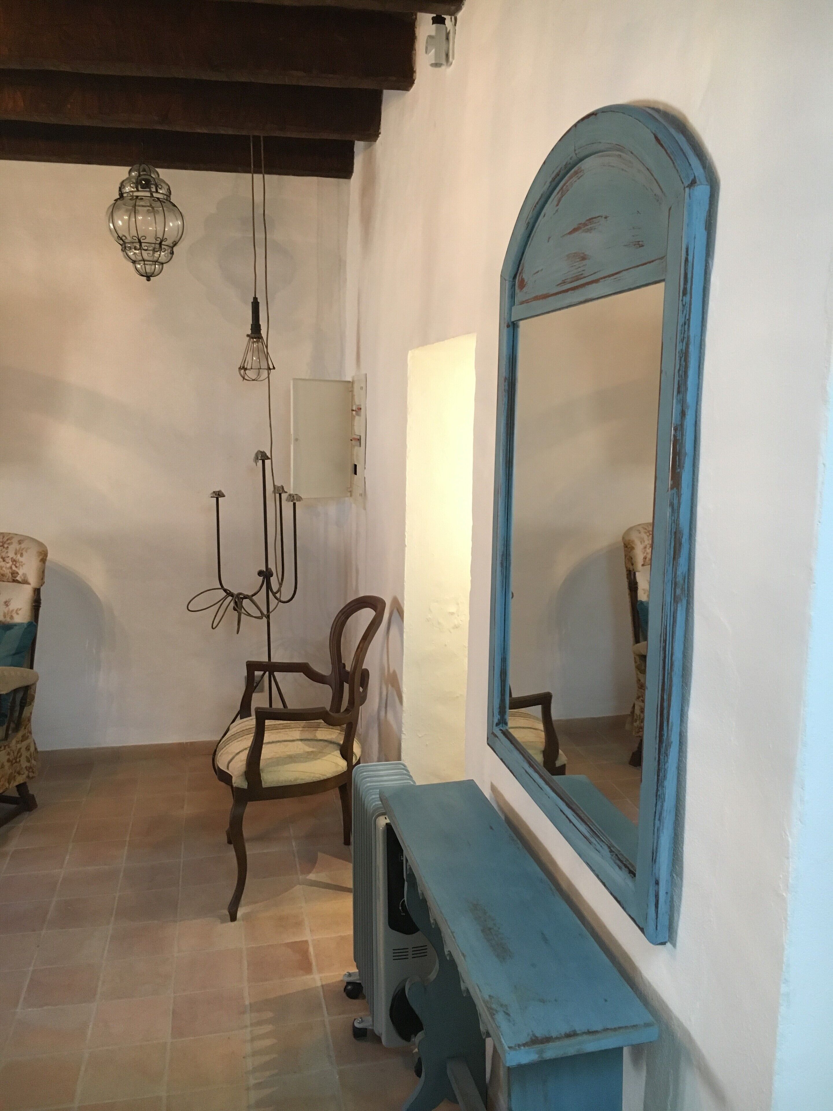 Una habitació amb una cadira de fusta, un mirall amb marc blau i una làmpada penjant.