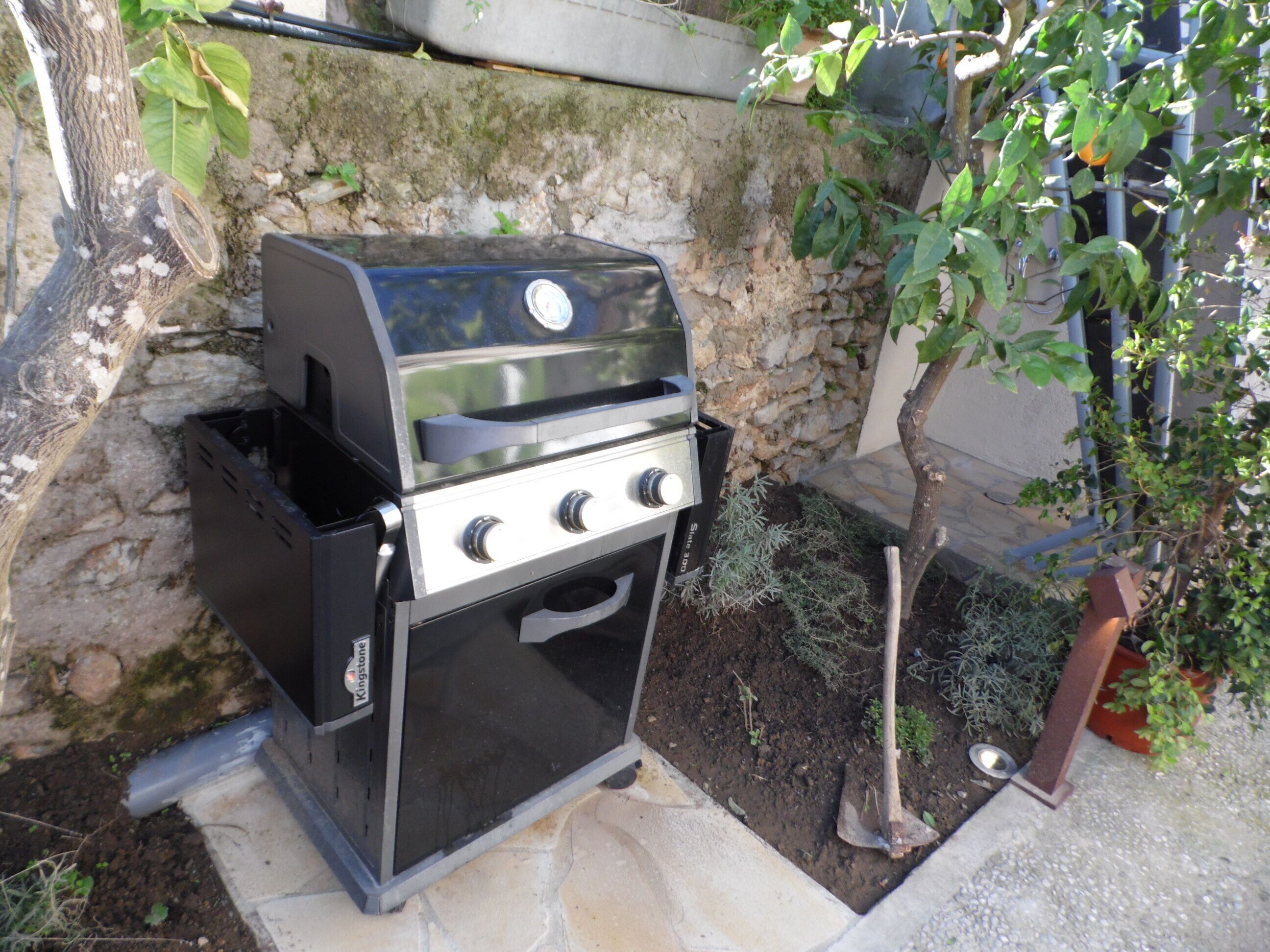 Una parrilla de gas portátil con pantalla digital, ubicada al aire libre frente a un muro de piedra.