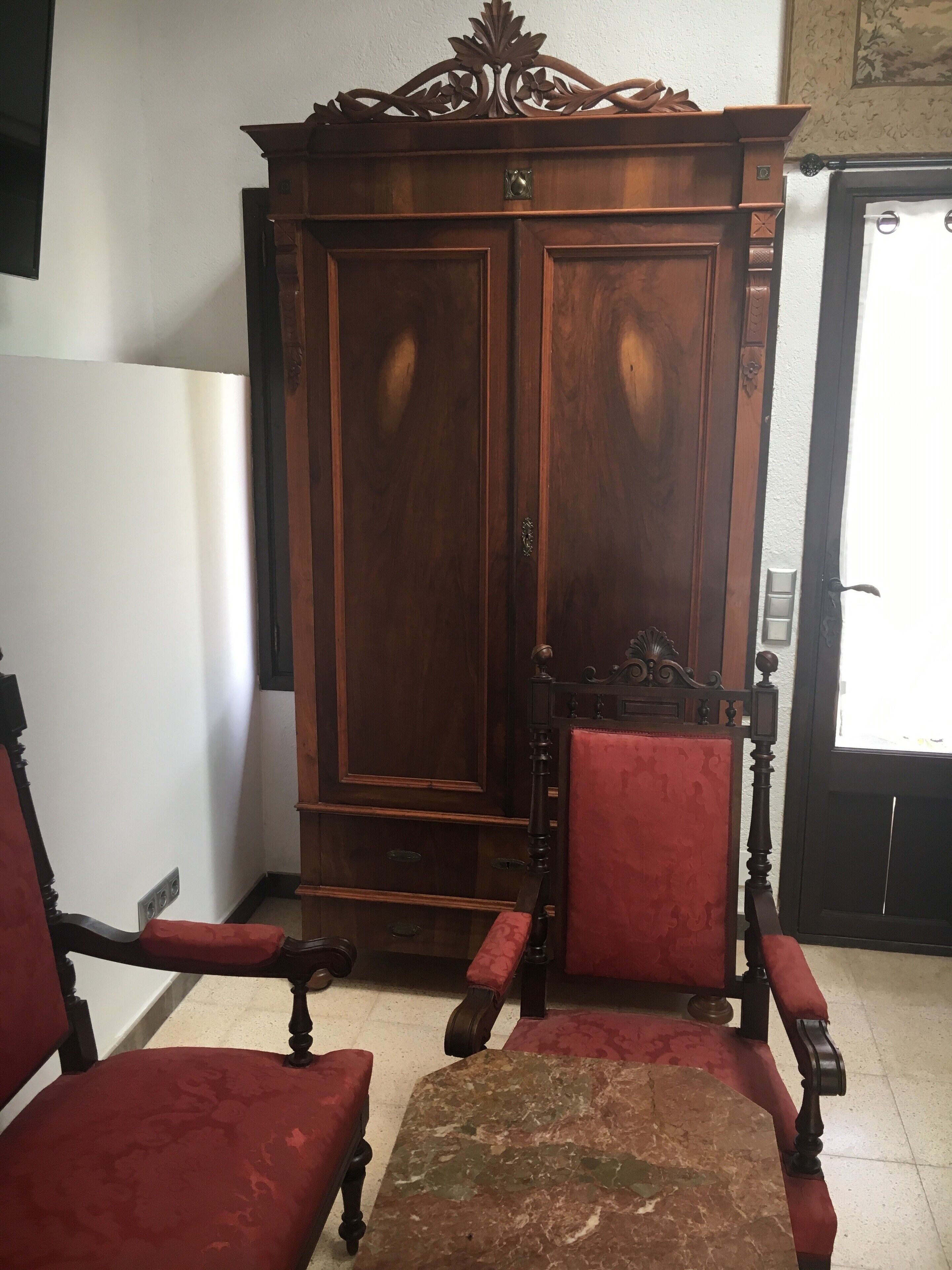 A wooden wardrobe with two doors and a red upholstered chair in front.