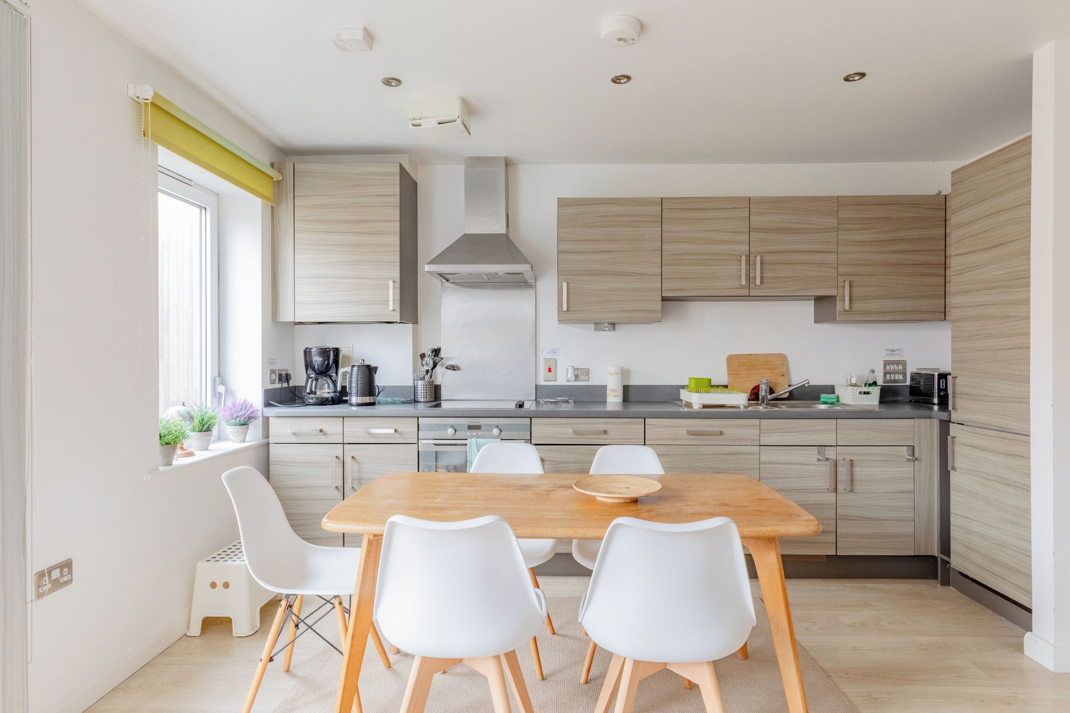 Une cuisine moderne avec une table à manger en bois, des chaises blanches et des meubles de rangement en bois clair.