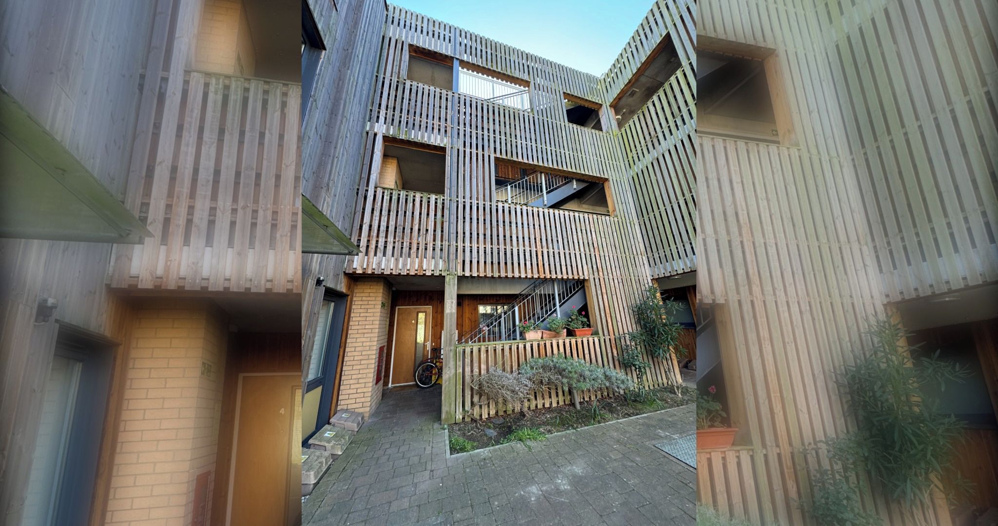 A multi-level residential building with a wooden facade, a central staircase, and a small garden area.