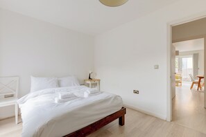 A minimalist bedroom with a bed, bedside table, and a view into an adjacent room.