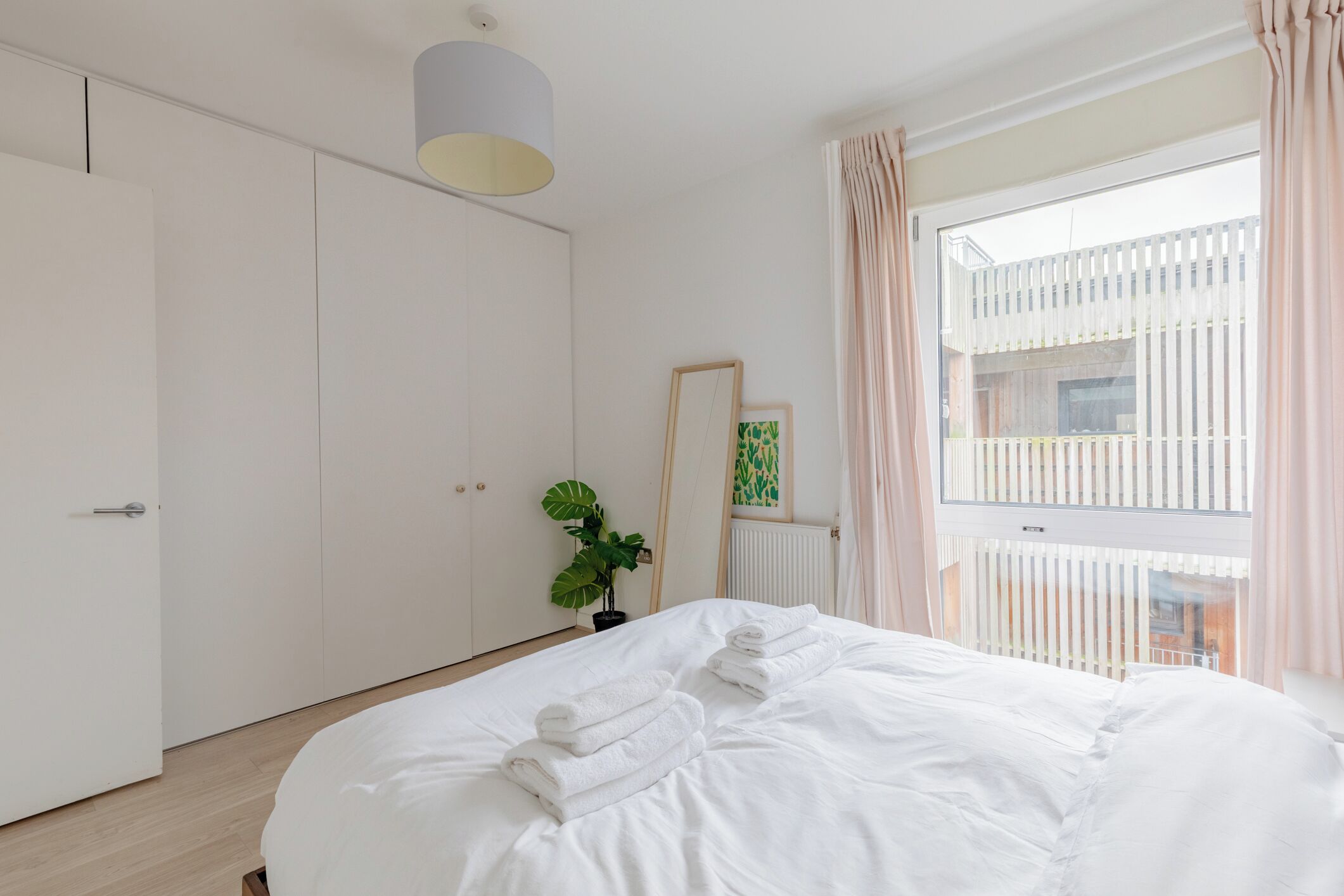 A bedroom with a bed, a potted plant, a mirror, and a window with curtains.