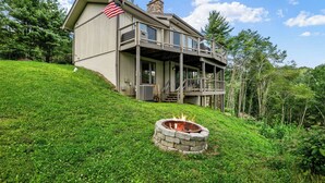 A two-story house with a stone fire pit in front, surrounded by lush greenery. - Mountain View, 3 minutes to downtown Banner Elk, easy access and ample parking!  (Beech Mountain)