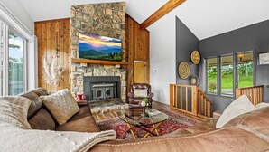 A cozy living room with a stone fireplace, leather sofa, and a large window offering a view of the outdoors. - Mountain View, 3 minutes to downtown Banner Elk, easy access and ample parking!  (Beech Mountain)