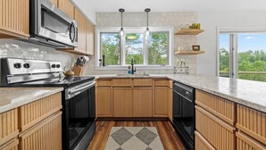A modern kitchen with wooden cabinets, stainless steel appliances, a large window, and a view of greenery. - Mountain View, 3 minutes to downtown Banner Elk, easy access and ample parking!  (Beech Mountain)