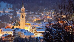 Un pueblo cubierto de nieve con una imponente torre de iglesia, rodeado de viviendas y árboles.