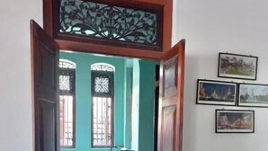 Ein Zimmer mit einem Bett, einem Esstisch und Stühlen. Es gibt Fenster mit dekorativen Eisengittern sowie eine Wand mit gerahmten Bildern.
