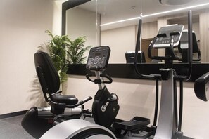 An exercise machine with a digital display, a chair, and a mirrored wall. - Palm Gate Hotel Suites (Riyadh)