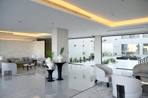 A modern hotel lobby with a spacious layout, a central column, and a view of the outdoor area. - Palm Gate Hotel Suites (Riyadh)