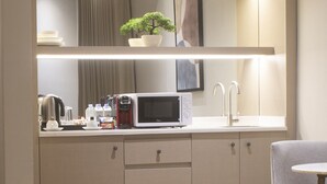 Una kitchenette moderna con microondas, hervidor y cafetera. Hay una pequeña planta en maceta sobre la encimera, y una foto enmarcada en la pared.