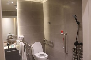 A bathroom with a white toilet, a hand dryer, a showerhead, and a grab bar. - Palm Gate Hotel Suites (Riyadh)