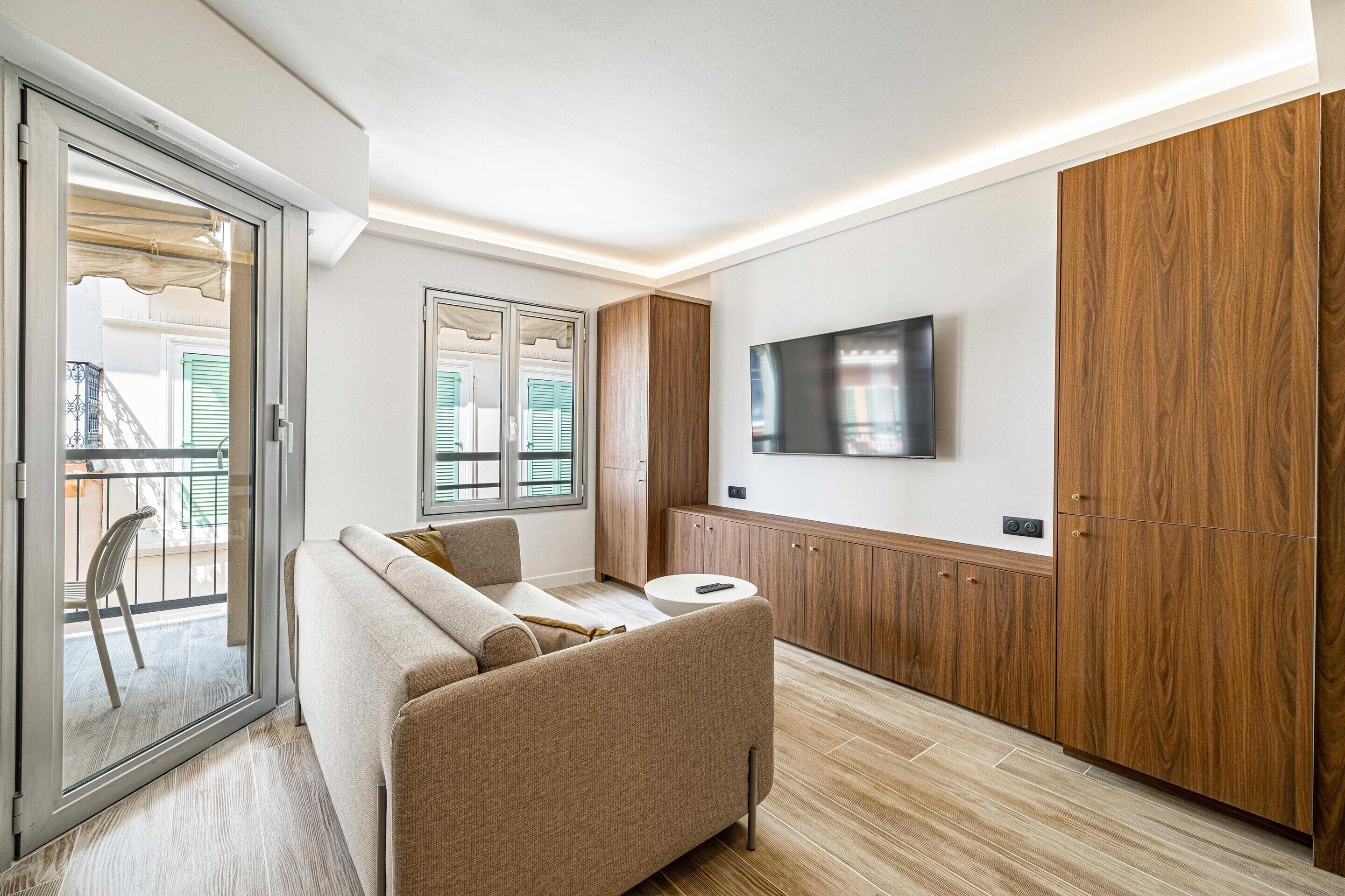 Una sala de estar moderna con un sofá, un televisor montado en la pared y armarios de madera.