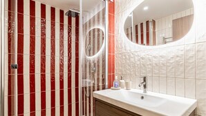 A modern bathroom with a glass-enclosed shower, a white sink with a mirror above it, and red-striped tiles on the walls. - Charming Flat - 2br-6p - Cannes (Cannes)
