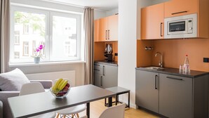 A compact kitchen with a dining area, a window with curtains, and a view of buildings outside. - Homaris Apartments Nibelungen (Frankfurt)