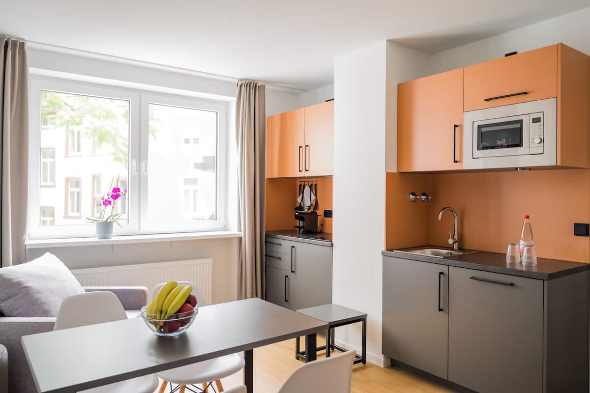 Cocina compacta con comedor, ventana con cortinas y vista a edificios.