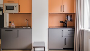 A compact kitchen with grey and orange cabinets, a microwave, a sink, and a small table. - Homaris Apartments Nibelungen (Frankfurt)