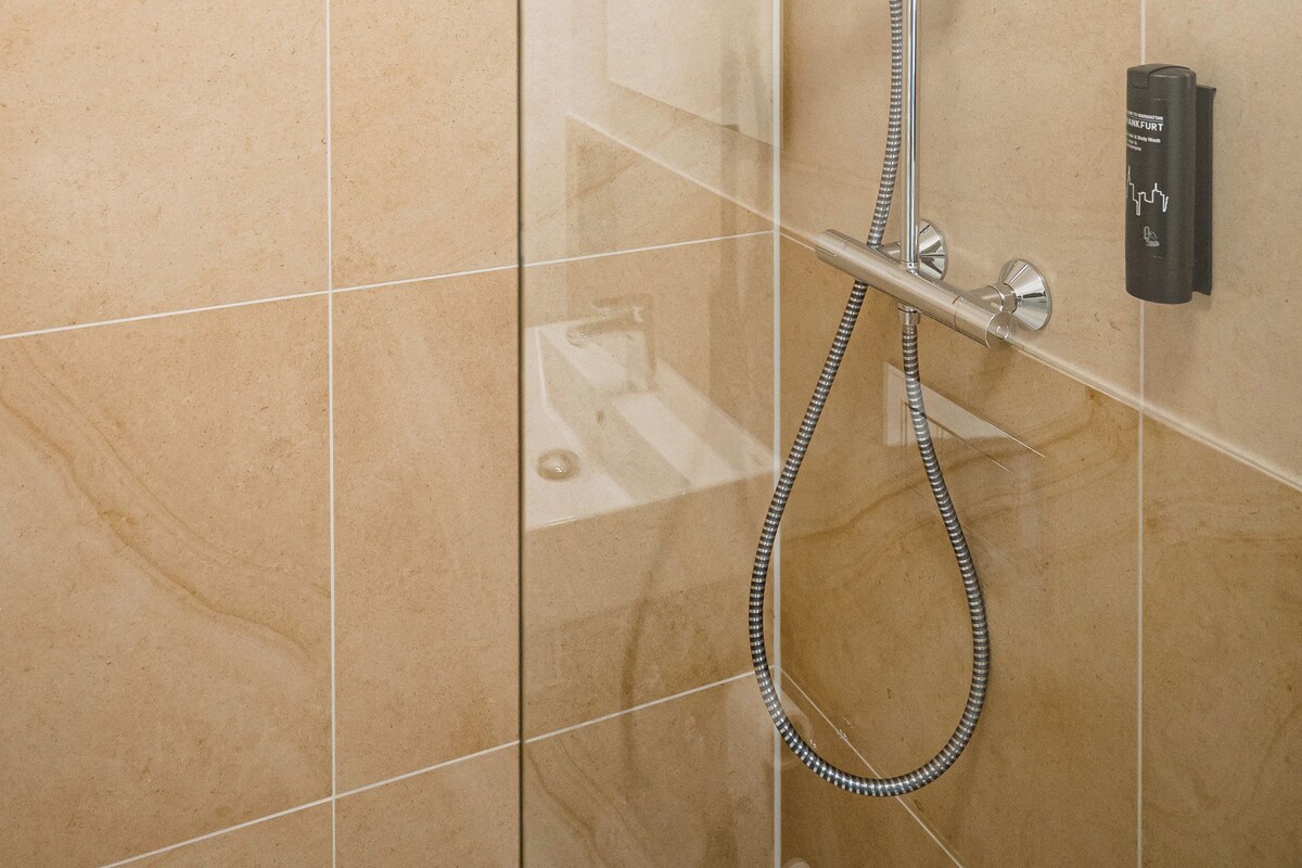 Ducha moderna con cabezal de ducha de mano y cabezal de ducha fijo en el techo, instalada en una pared con baldosas grandes y de color claro.