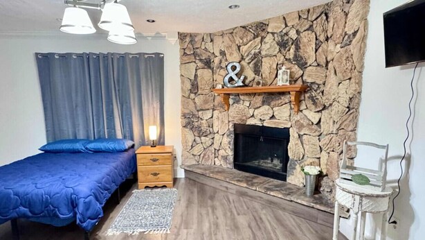 A bedroom with a bed, a wooden nightstand, a stone wall, a fireplace, and a television. - Entire Spacious 4 BR Home for Teams (Port Arthur)