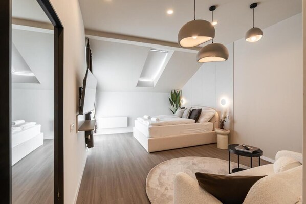 A modern bedroom with a large bed, bedside tables, a round seating area, and a skylight.