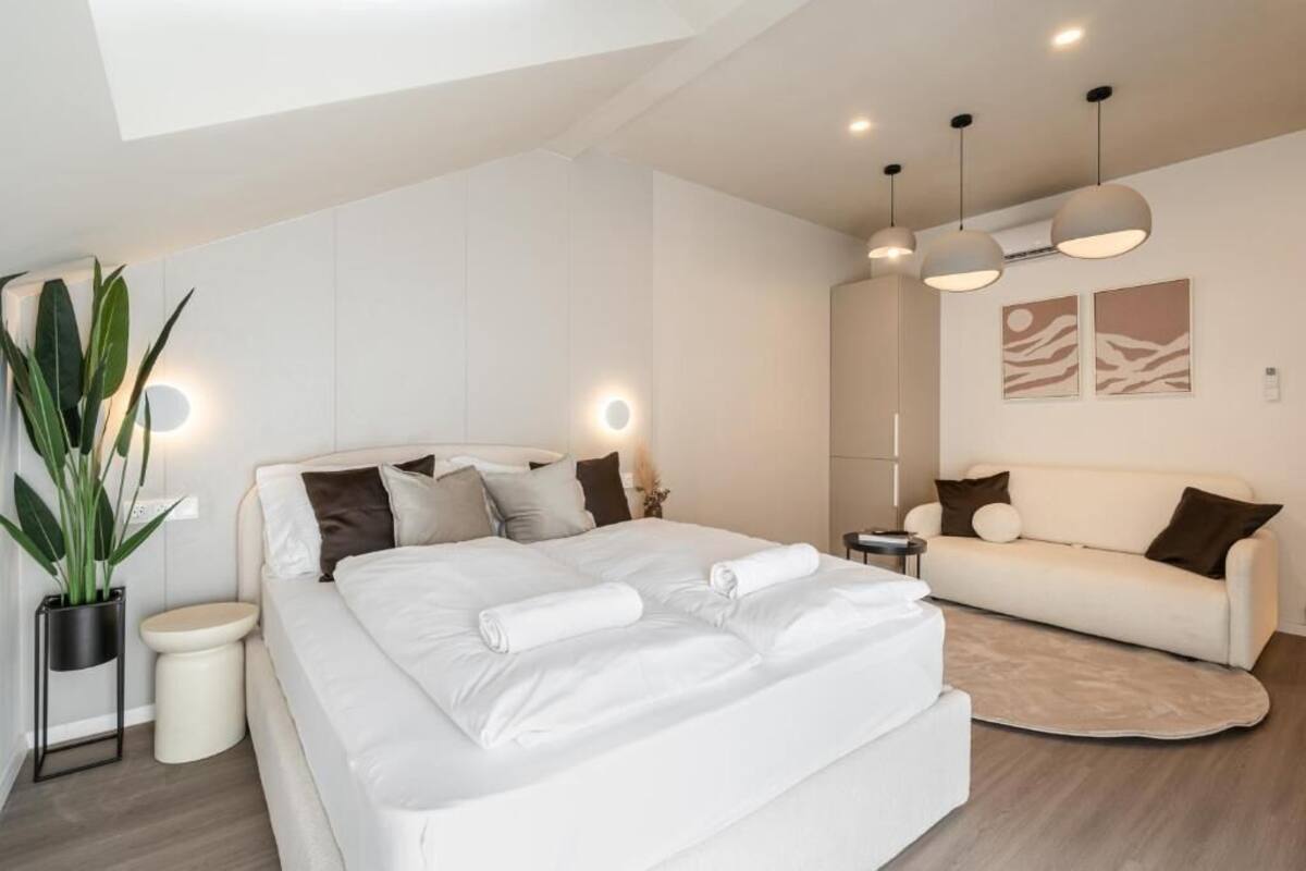 Une chambre d’hôtel moderne avec un grand lit, un canapé, une plante en pot et un luminaire fixé au plafond.