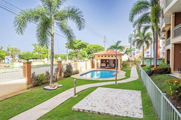 A residential area with a swimming pool, palm trees, and a small building with a red roof.