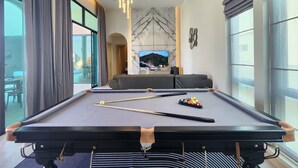 Un salón moderno con mesa de billar, televisor y un amplio ventanal con cortinas.