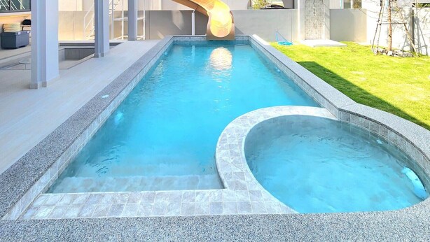 Una piscina con tobogán, rodeada por un edificio moderno con pasarelas arqueadas y un cielo despejado.