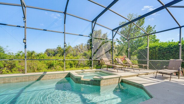 A pool with clear water, surrounded by a covered area with lounge chairs and a view of greenery.