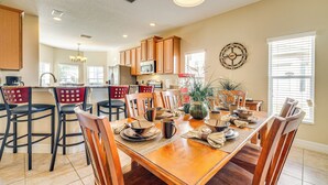 A spacious kitchen with wooden cabinets, a dining area with a wooden table and chairs, and a large window with blinds.