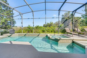 Et udendørs swimmingpool med et overdækket område, omgivet af liggestole og udsigt til en bakke.