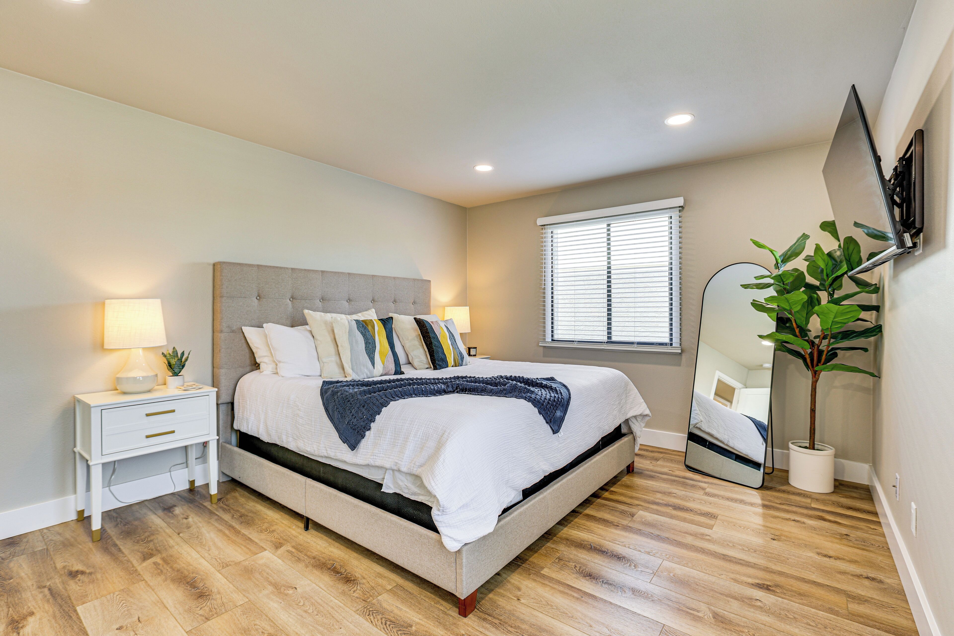 A bedroom with a bed, nightstand, lamp, potted plant, and a mirror.