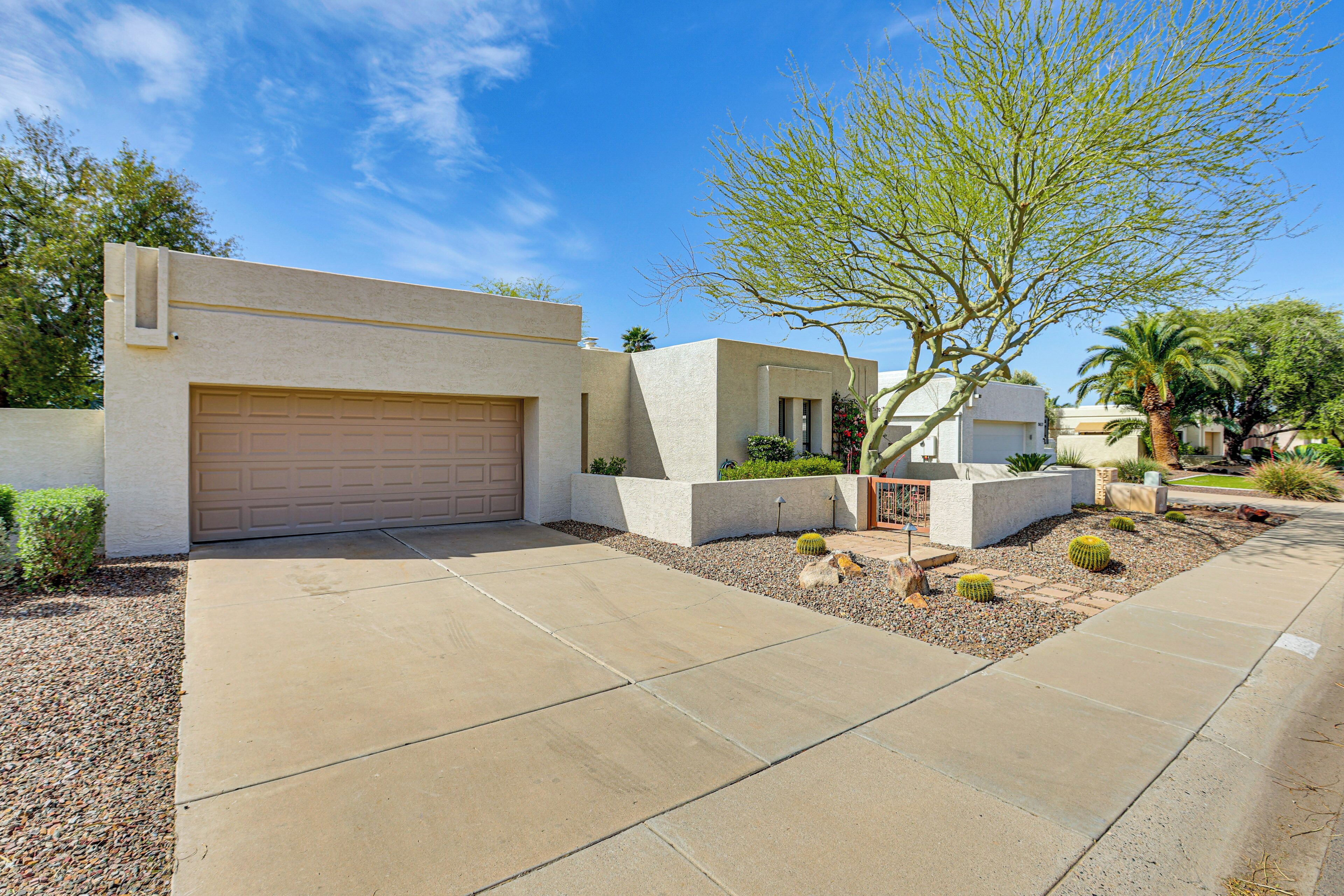 A modern house with a garage, a landscaped garden with cacti and a palm tree, and a clear blue sky.