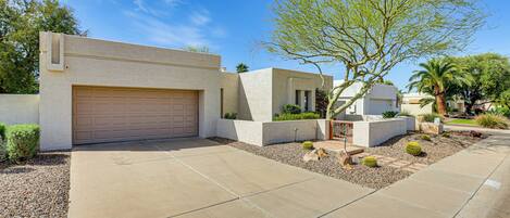 A modern house with a garage, a landscaped garden with cacti and a palm tree, and a clear blue sky.