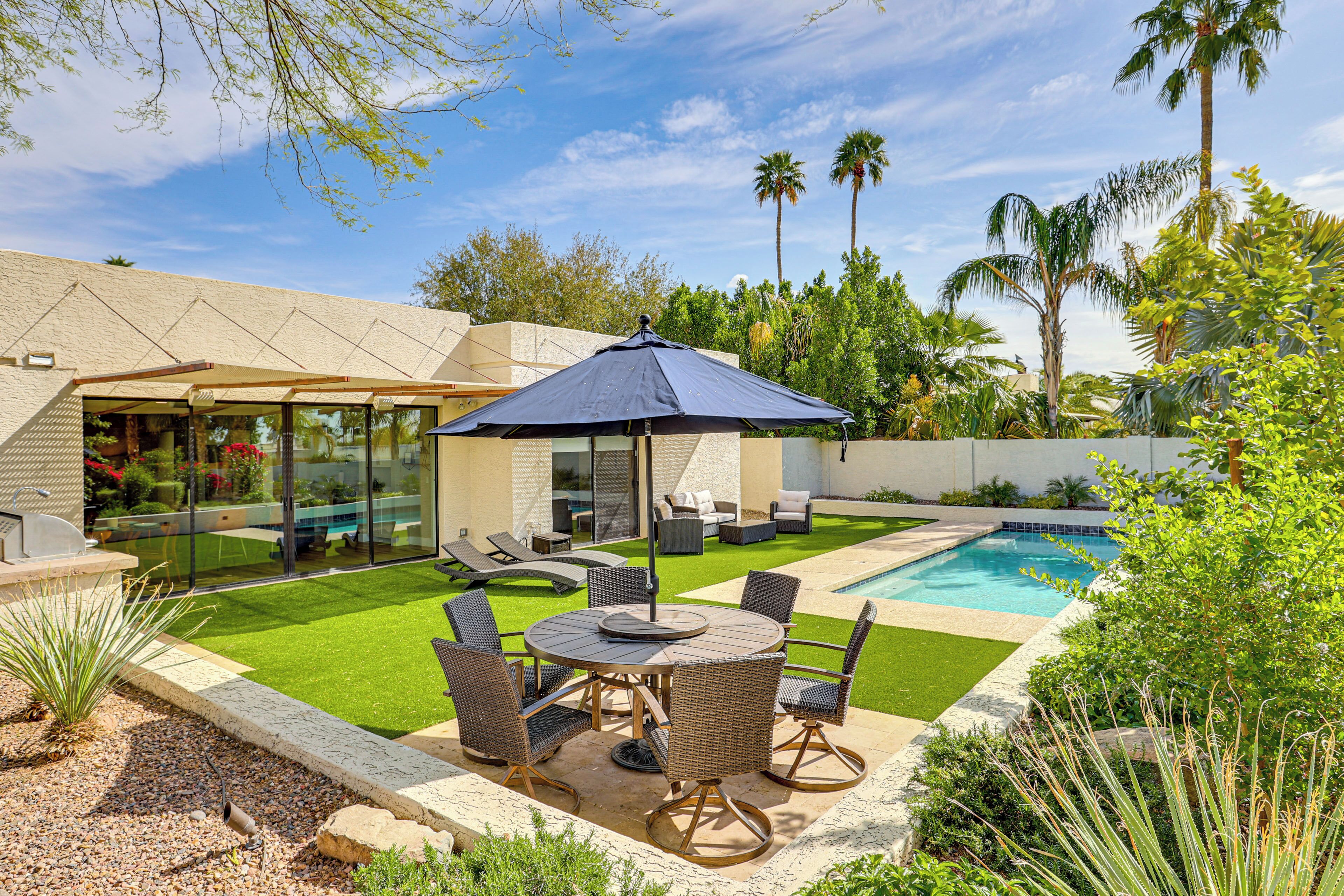 A backyard with a pool, outdoor furniture, and a patio area.