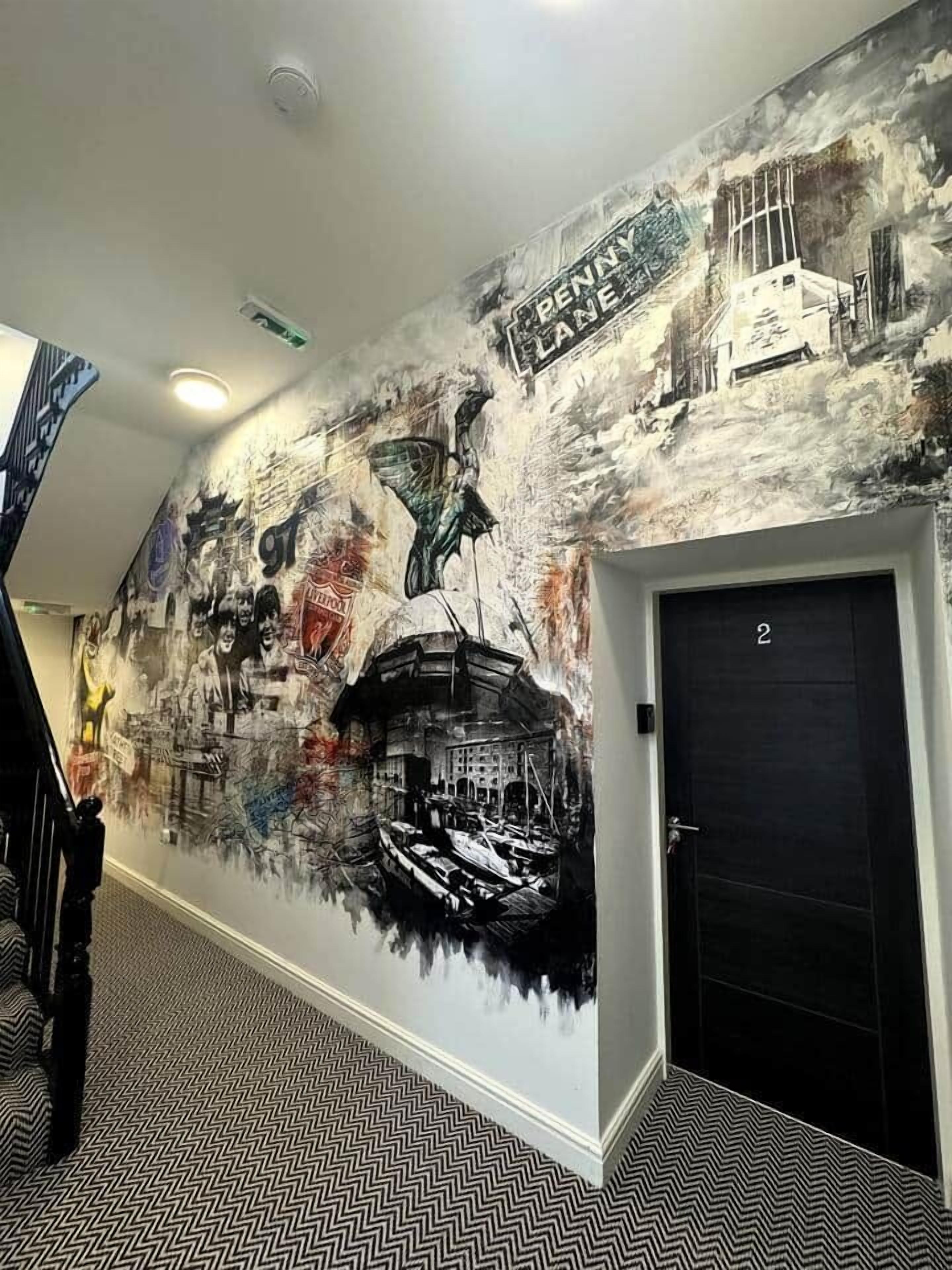 Un pasillo con un mural que representa un paisaje urbano, una escalera y una puerta marcada con el número 2.