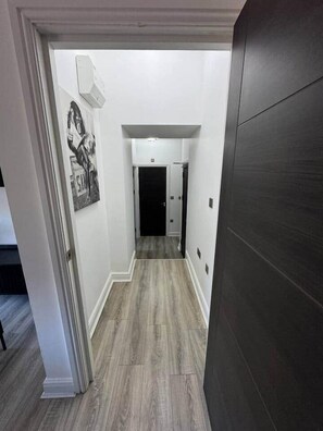 Un couloir doté d’un plancher en bois, de murs blancs et d’une porte en bois foncé.