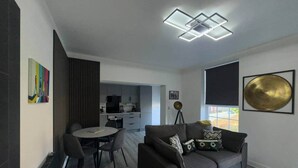 Zona d'estar moderna amb sofà, taula de menjador i cuina al fons.