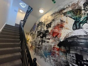 A staircase with patterned carpet and a wall with a mural featuring a football club emblem and a bird. - Apt 4, 38 Everton Road (Liverpool)