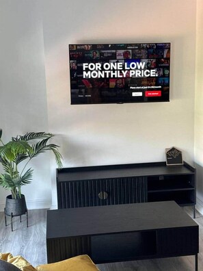 Un salon moderne avec un téléviseur à écran plat fixé au mur, une table basse en bois foncé et une plante en pot.
