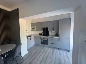Une cuisine moderne avec des meubles gris, un four à micro-ondes, une cuisinière et un coin repas comprenant une table et des chaises.