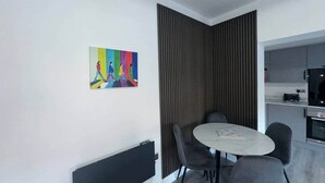 Zona pranzo moderna con tavolo e sedie, cucina sullo sfondo e un quadro astratto colorato appeso al muro.