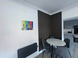 Un comedor moderno con una mesa y sillas, una cocina al fondo y un cuadro abstracto de colores en la pared.
