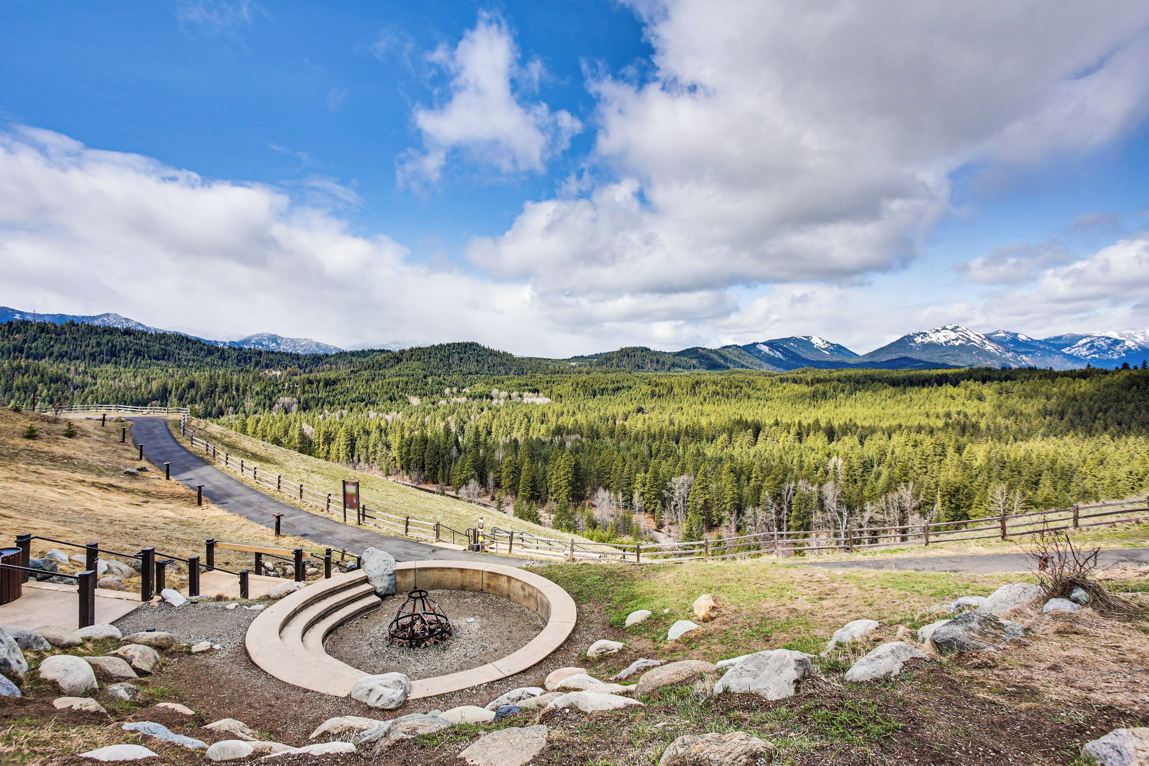 A scenic view of a mountainous landscape with a circular stone structure, a winding road, and a wooden fence.
