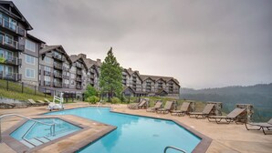 A swimming pool with lounge chairs and a view of a multi-story building with balconies. - Stay & Play: Suncadia Resort Condo in Cle Elum (Cle Elum)