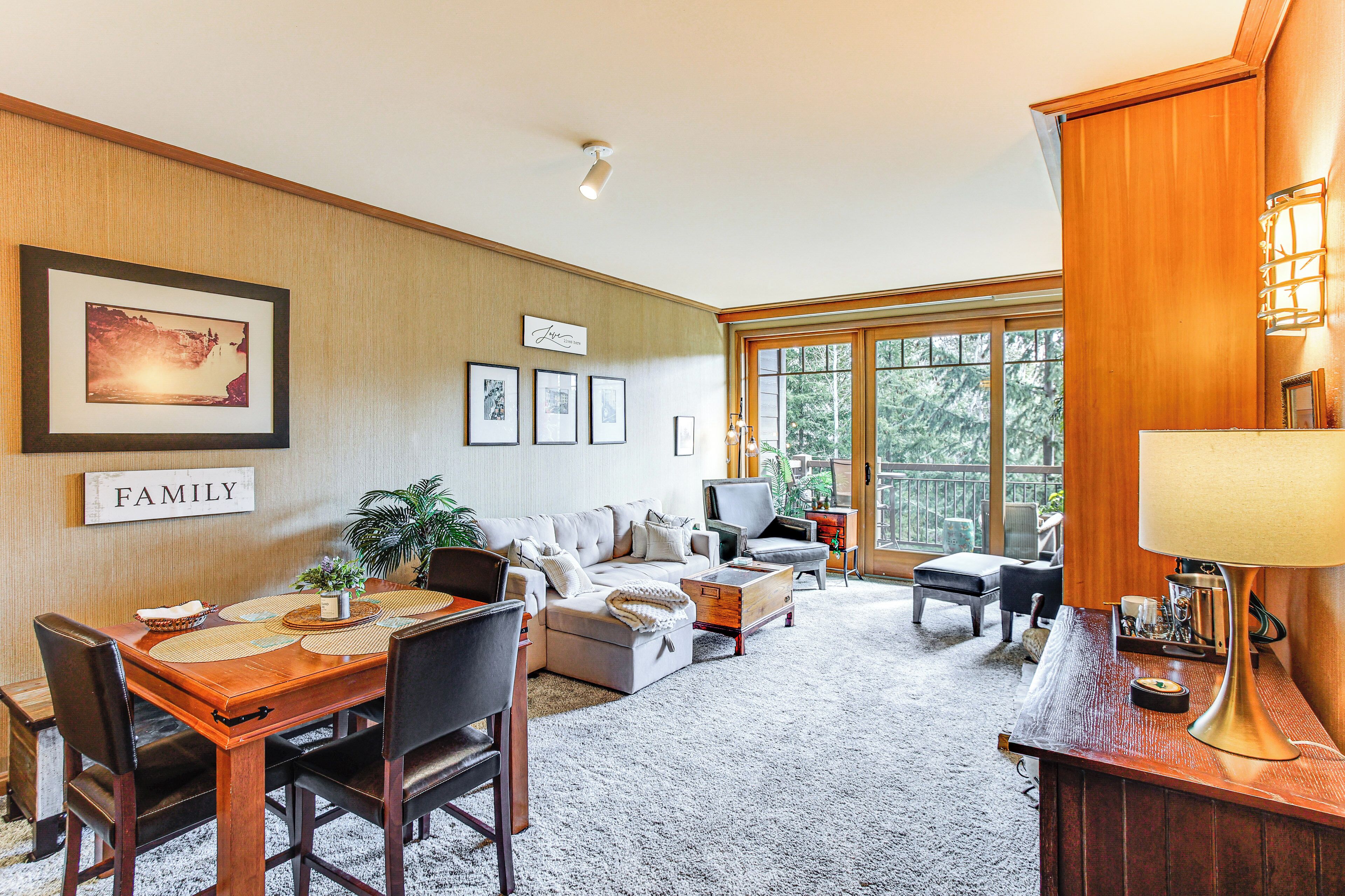 A spacious living room with a wooden dining table, comfortable seating, and a large window offering a view of the outdoors.