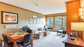 A spacious living room with a wooden dining table, comfortable seating, and a large window offering a view of the outdoors.