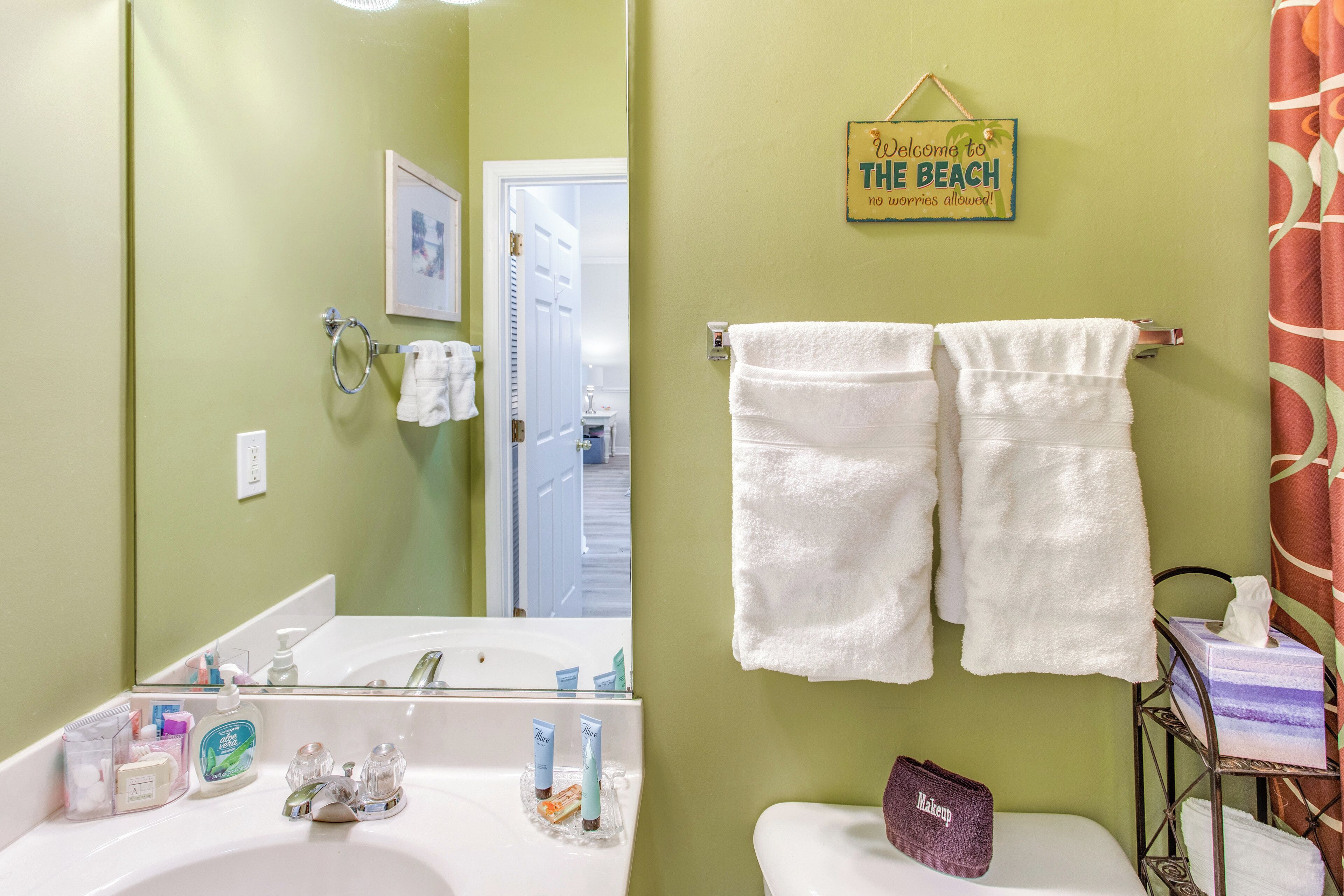 Un baño con lavamanos, espejo, toallero y un cartel que dice 'Welcome to the Beach'.